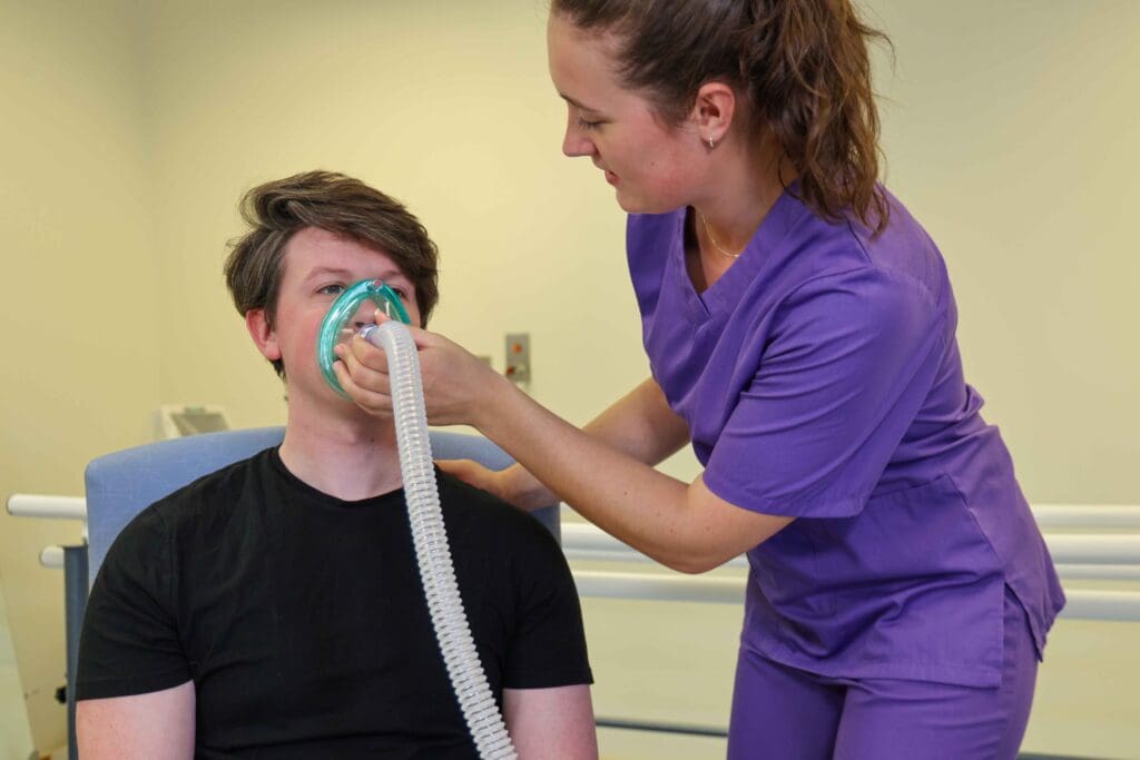 A man breathing with a secretion clearance device with a nurse in the background